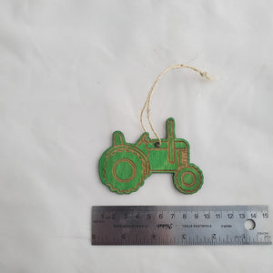 Green decorative tractor ornament with a string, next to a ruler for scale, on a white background